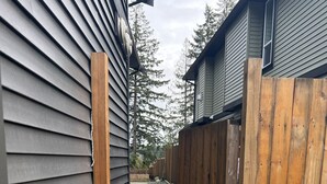 Un sendero estrecho que conduce a una casa con revestimiento gris y una valla de madera.
