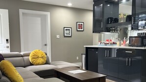 Una sala de estar moderna con un sofá seccional gris, una mesa de centro de madera, y una zona de cocina con armarios negros y un microondas.