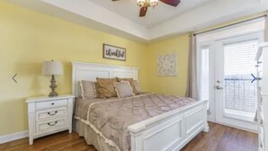 A bedroom with a bed, nightstand, lamp, ceiling fan, and a door with a window.
