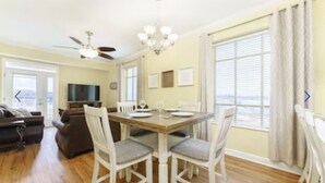 A dining area with a wooden table and white chairs, a ceiling fan, and a chandelier.
