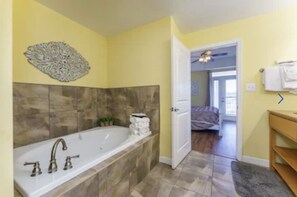 A bathroom with a large bathtub, a decorative wall piece, and a door leading to another room. - Gorgeous 3 bed, 2 bath condo on the river! (Sevierville)