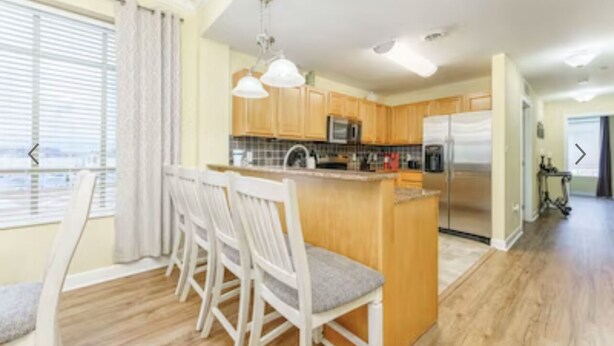 A modern kitchen with wooden cabinets, a central island with seating, and a view of the city through large windows.
