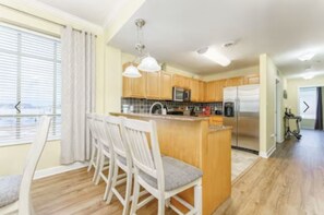 A modern kitchen with wooden cabinets, a central island with seating, and a view of the city through large windows. - Gorgeous 3 bed, 2 bath condo on the river! (Sevierville)