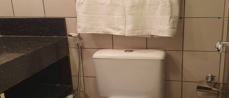 Un baño con inodoro, un cesto de basura negro y una toalla colgada en la pared.
