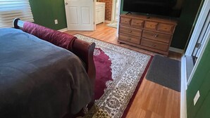 A bedroom with a bed, a television, a dresser, and a door leading to another room.