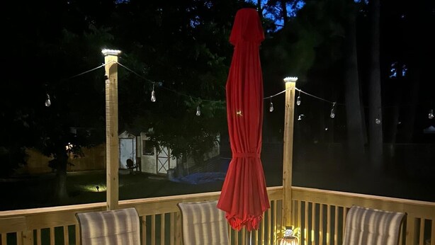 An outdoor dining area with a table and chairs, string lights, and a red umbrella.