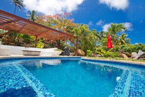 A swimming pool with clear blue water, surrounded by tropical plants and a wooden pergola. - Villa Honohitu w/pool, bbq outdoor space, and mini bar (Takitumu District)