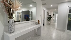 Um corredor moderno com um console branco, um espelho grande e um vaso com plantas secas.