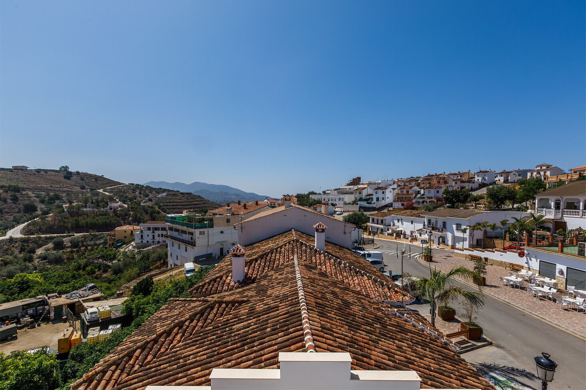 Une ville perchée sur une colline, avec des toits couverts de tuiles en terre cuite, des bâtiments blancs et un ciel d’un bleu limpide.