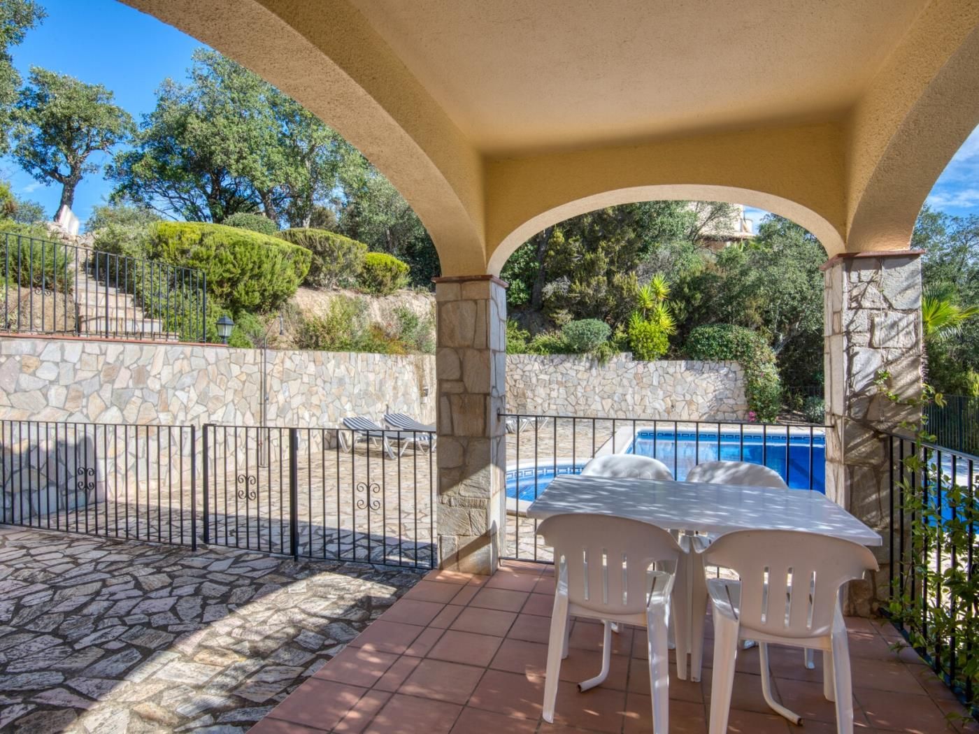 A covered outdoor area with a stone wall, a pool, and two white plastic chairs.