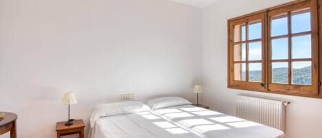 Une chambre avec deux lits, une fenêtre, un radiateur et une petite table avec une lampe.