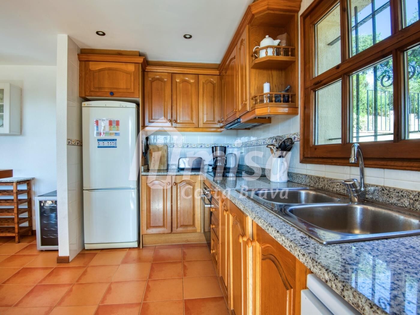 A kitchen with wooden cabinets, a stainless steel sink, and a refrigerator.