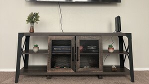 A flat-screen TV mounted on a wall above a dark wooden entertainment center with two small potted plants and a gaming console. - Scottsdale Couples Getaway| Pool & Hot Tub| Scenic (Scottsdale)