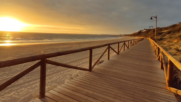 A wooden boardwalk leading to a beach with a sunset in the background.