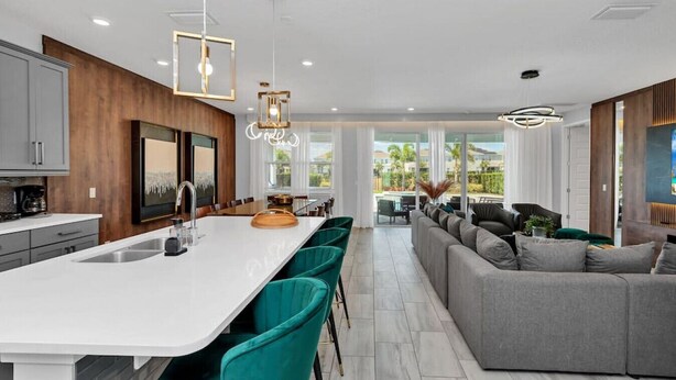 Une cuisine moderne dotée d’un grand îlot central, de chaises de couleur turquoise et d’un canapé gris, le tout dans un espace de vie lumineux agrémenté de grandes fenêtres.