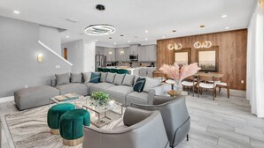 Un salon moderne avec un canapé d’angle gris, des poufs turquoise et une table basse en verre.