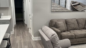 Un salon moderne avec un canapé gris, une table basse en bois et un tableau représentant une jetée.