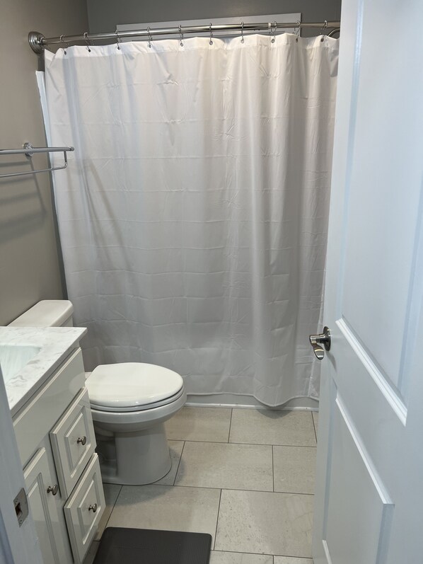 Ein Badezimmer mit Toilette, weißer Duschvorhang, Marmorwaschbecken und einer Tür.