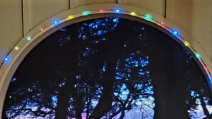 Un comedor con una mesa dispuesta para dos, que ofrece vistas a través de una ventana con arco decorativo y guirnaldas de luces.