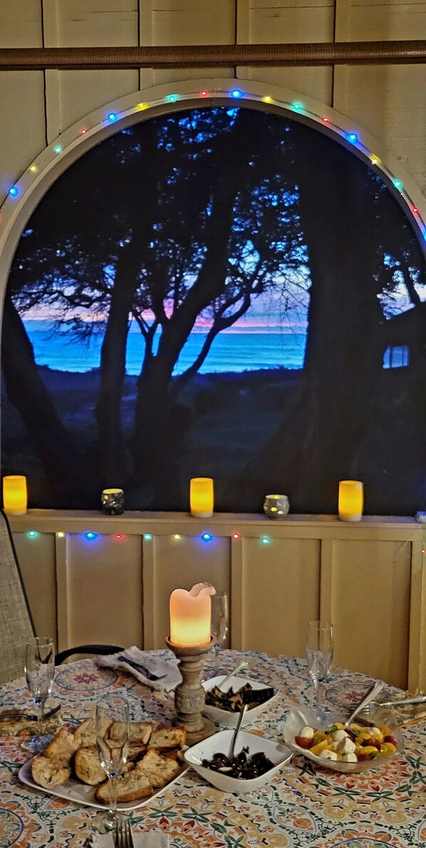 A dining area with a table set for two, featuring a view through a window with a decorative arch and string lights.