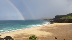 A beach with a rainbow, clear sky, and ocean waves.