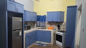 A compact kitchen with blue cabinets, a stainless steel refrigerator, a microwave, a stove, and a tiled backsplash. - 2 BR w/ AC APT near Grand Anse Beach -15 mins walk, 10 mins away from airport. (The Lime)