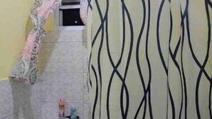 A bathroom with a toilet, a shower curtain with a wavy pattern, and a towel hanging on the wall. - 2 BR w/ AC APT near Grand Anse Beach -15 mins walk, 10 mins away from airport. (The Lime)