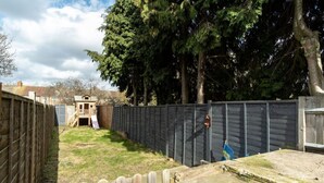 Un patio trasero cercado con una casita de juegos de madera y un árbol alto.