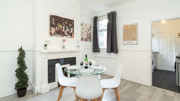 Un comedor con una mesa redonda de vidrio, sillas blancas, una chimenea y un mapa de Los Ángeles en la pared.