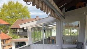 Un patio techado con una mesa y sillas, vistas a casas vecinas y piso de baldosas.