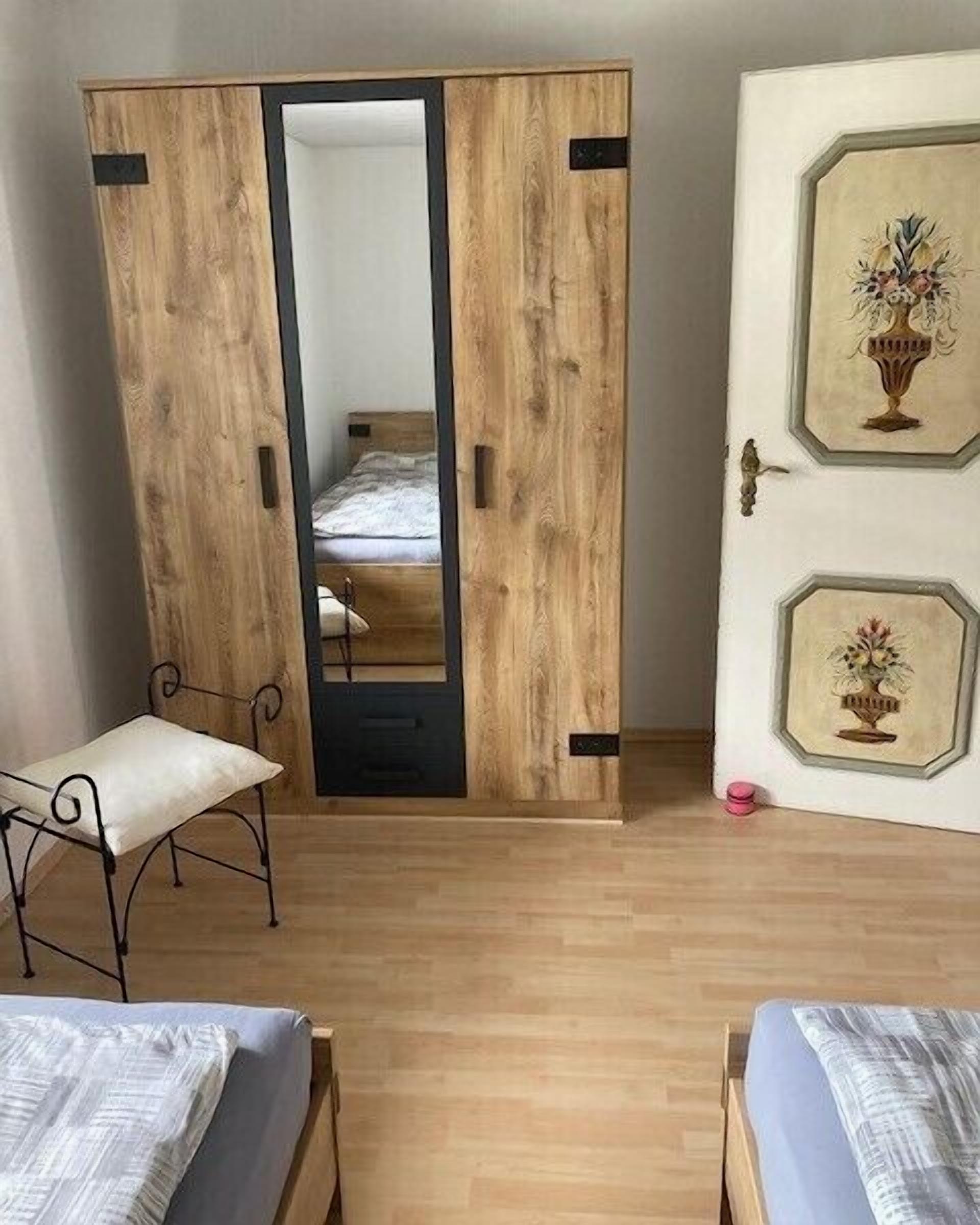 A bedroom with a wooden wardrobe, a bed, a chair, and a door with framed artwork.