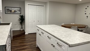 A modern kitchen with white cabinetry, a marble countertop, and a wooden dining table. - Feel at home in This 2 Bedroom Basement Suite (Kamloops)