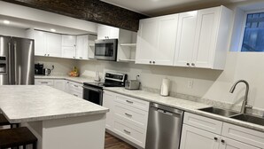 A modern kitchen with white cabinetry, stainless steel appliances, and a central island. - Feel at home in This 2 Bedroom Basement Suite (Kamloops)