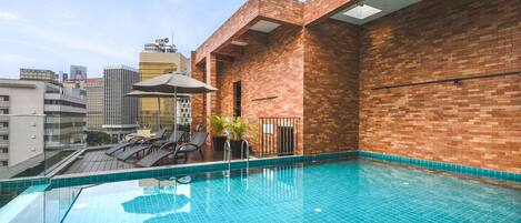 A rooftop swimming pool with a city view, lounge chairs, and a potted plant.