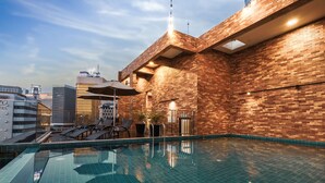 Una piscina interior con suelo de baldosas y pared de ladrillo. Hay sillones de descanso y una sombrilla.