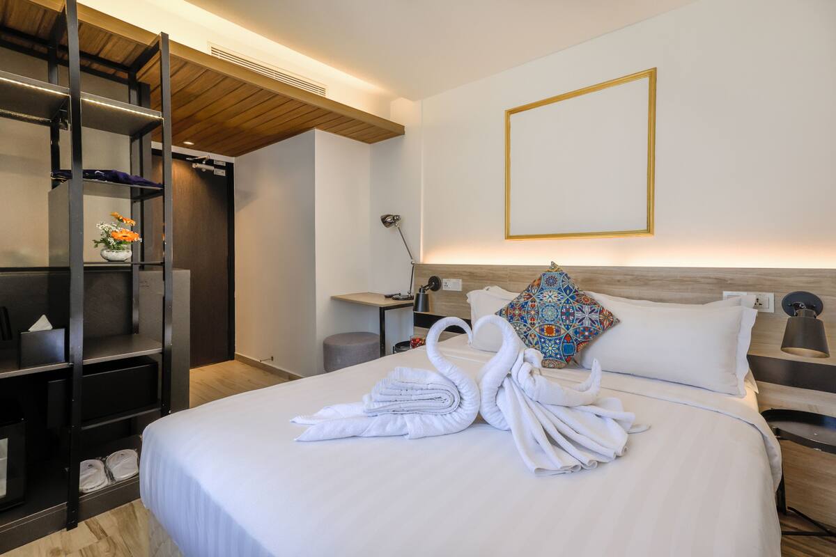 A hotel room with a bed, a wardrobe, a bedside table with a lamp, and a wall-mounted picture frame.