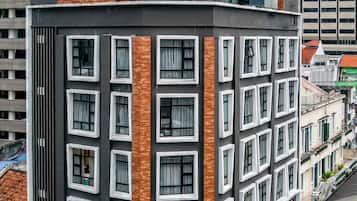 A multi-story building with a modern design, featuring a mix of brick and concrete facades, large windows, and a rooftop terrace with outdoor seating.