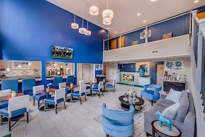 Eine großzügige Lobby mit blau-weißer Farbgestaltung, mit einer Sitzecke mit blauen Stühlen und Tischen, einem grauen Sofa und einer Treppe zu einer oberen Ebene.