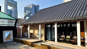 A modern outdoor seating area with wooden flooring and a metal roof, overlooking a cityscape with tall buildings. - WOO MI GWAN HOTEL (Seoul)