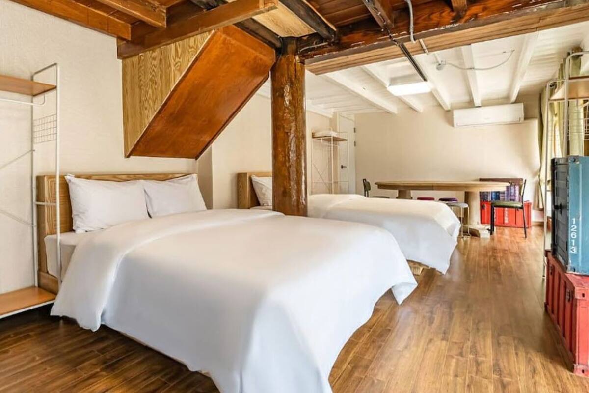 Quarto com duas camas, vigas de madeira, piso de madeira e uma televisão.