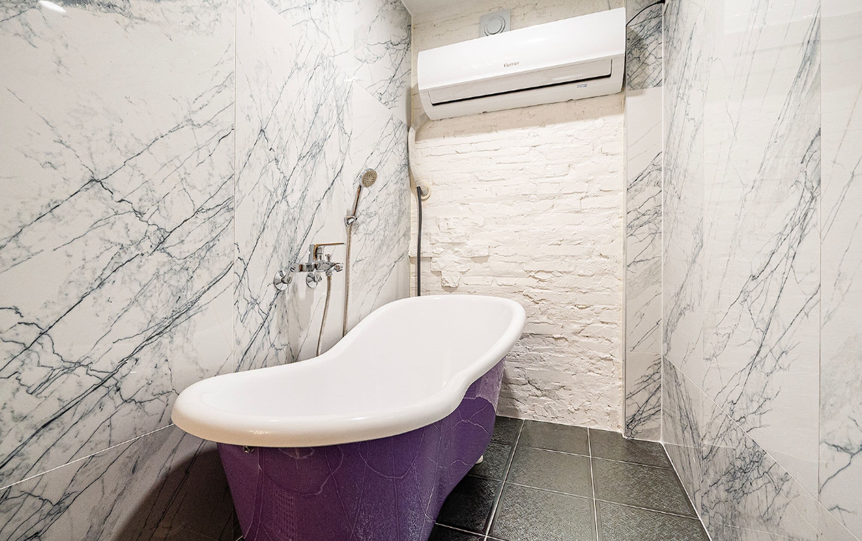 A bathroom with a marble wall, a white air conditioning unit, and a purple bathtub.