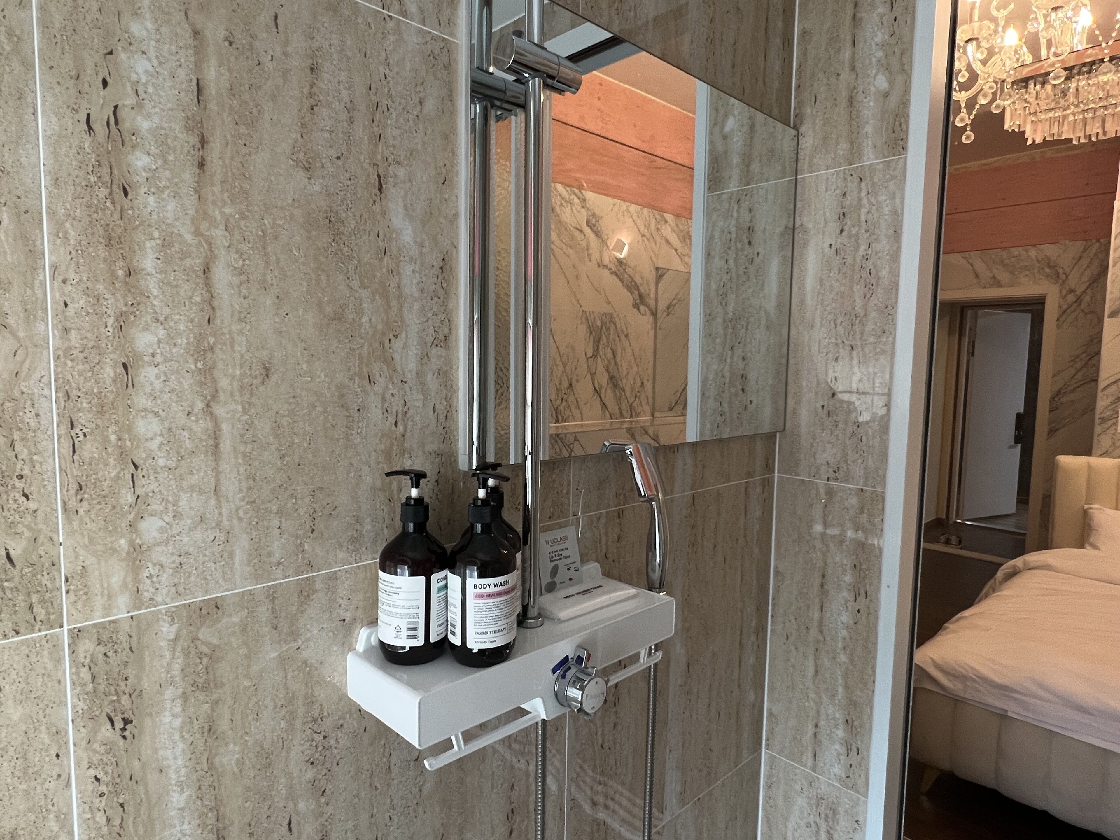 Un bagno moderno con una parete in marmo, un lavabo incassato e una doccia. Sul lavabo ci sono due flaconi di bagnoschiuma.