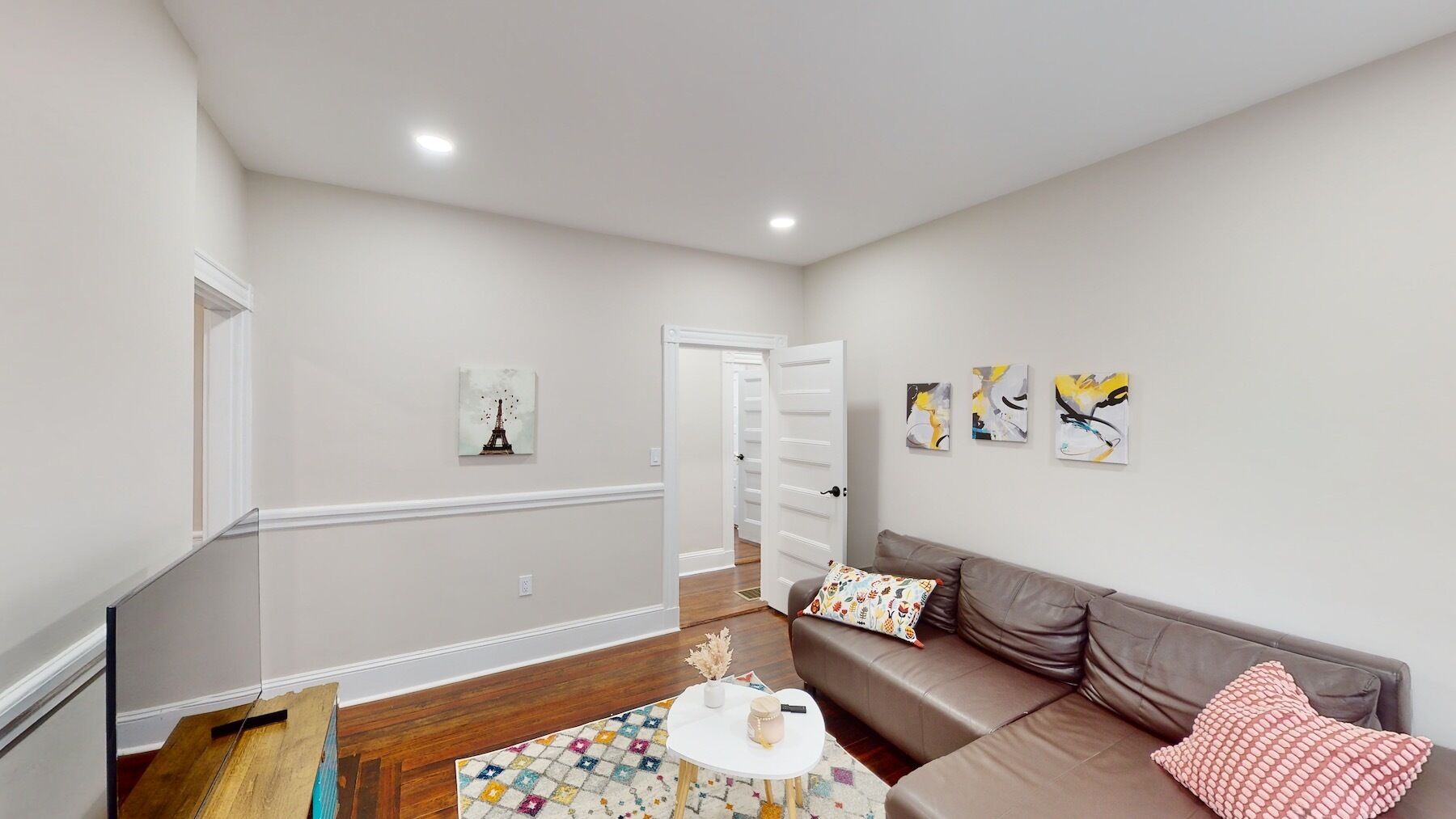 A modern living room with a brown leather sofa, a small white table with a colorful rug, and abstract wall art.