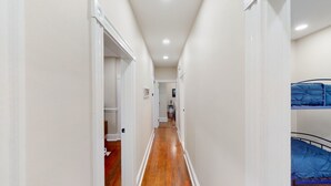 Un couloir étroit avec un plancher en bois, des murs blancs et un lit superposé sur le côté droit.
