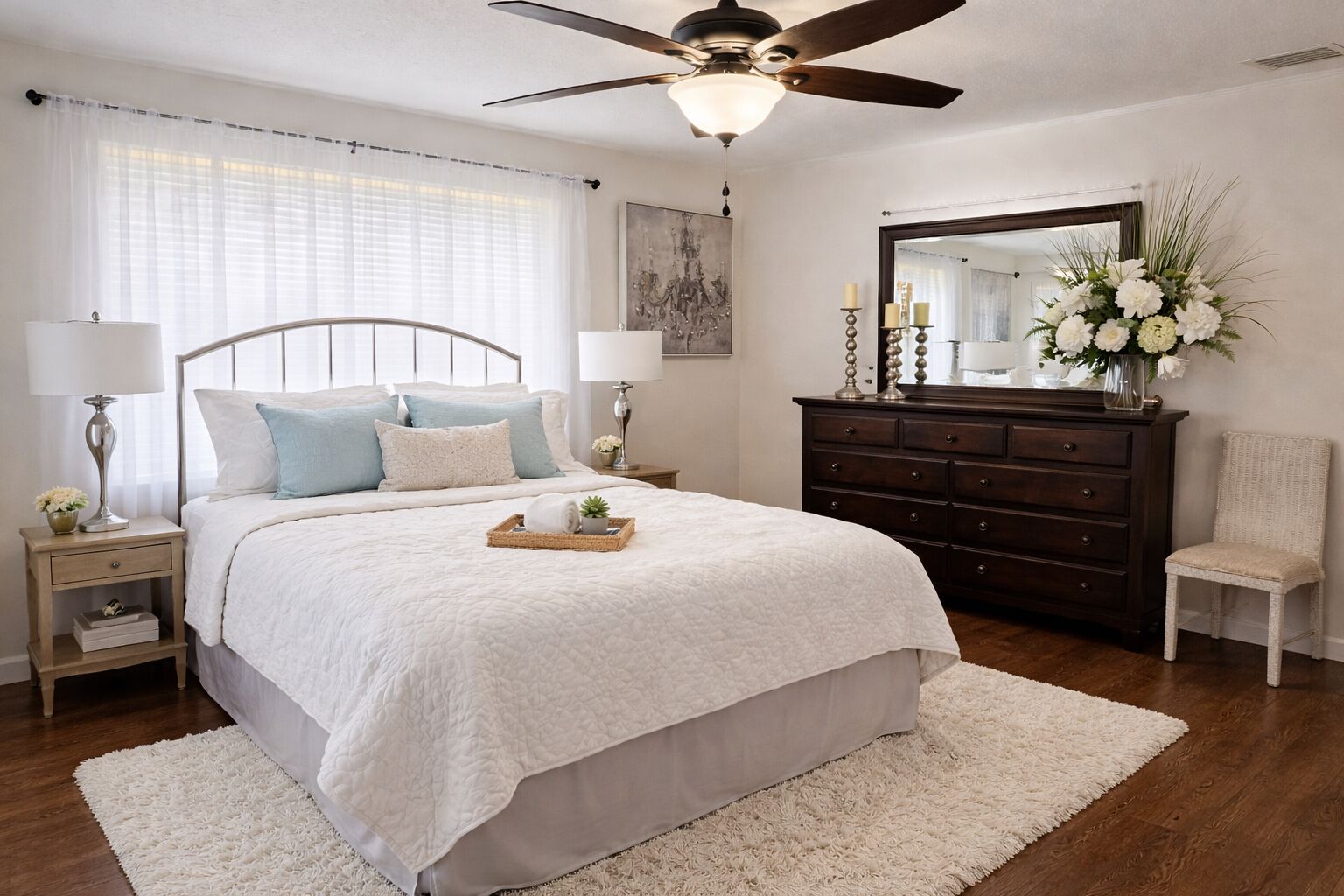 A bedroom with a bed, nightstands, a dresser, a chair, a ceiling fan, and a mirror.