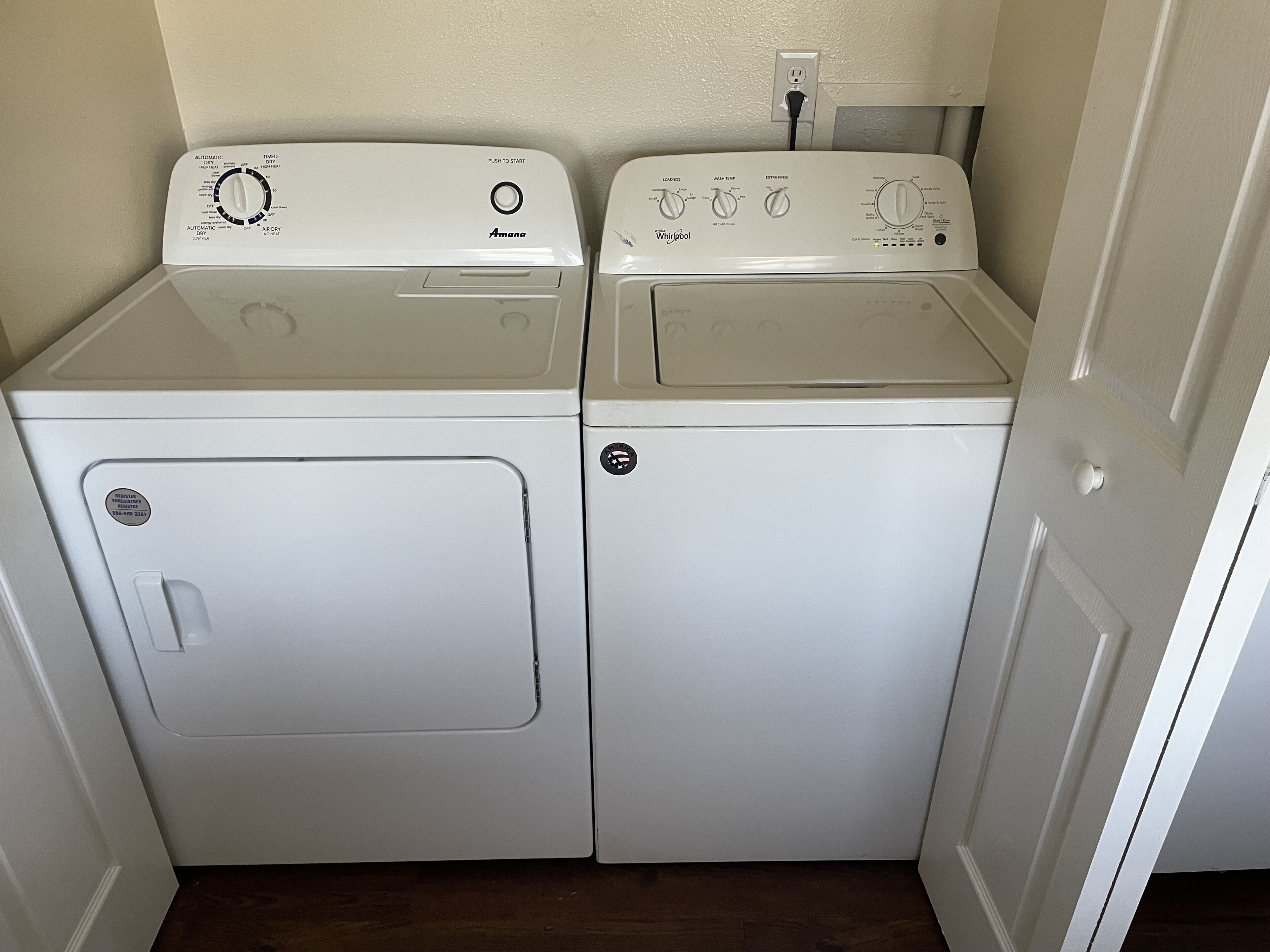 A laundry room with two stacked washers and dryers, a power outlet above the dryers, and a door to the right.