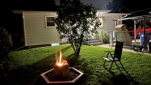 A backyard with a fire pit, a lawn chair, and a house. - Lovely cottage with fenced in back yard (Wausau)