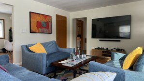 A living room with a blue sofa, a coffee table with a welcome sign, a TV, and a door leading to another room. - Lovely cottage with fenced in back yard (Wausau)