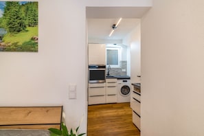 Una cucina compatta con lavatrice, una panca in legno e un quadro che raffigura una foresta.