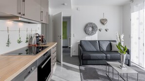 Een moderne keuken met een inbouwoven, een eethoek met een zwarte bank en een salontafel, en een woonkamer met een grijze bank en decoratieve wandkunst.